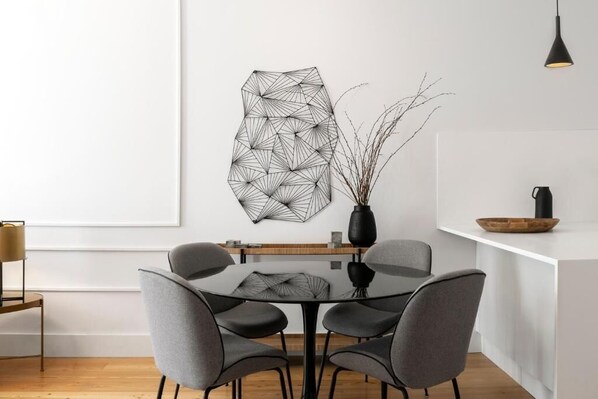 A modern dining area with a geometric wall art piece, a vase with branches, and a minimalist table setting.