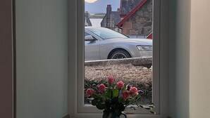 A window with a view of a parked car, a stone building, and a mountain in the background. - The Coorie Inviting 1-bed Apartment in Oban (Oban)