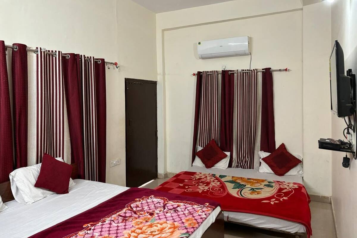 A hotel room with two beds, red and white striped curtains, a ceiling fan, an air conditioning unit, and a TV mounted on the wall.
