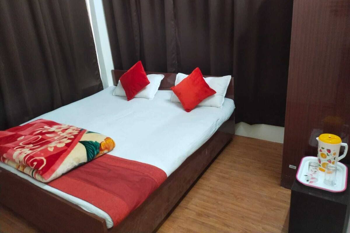 A hotel room with a bed, red and white pillows, a red blanket, and a tray with a mug and glasses.