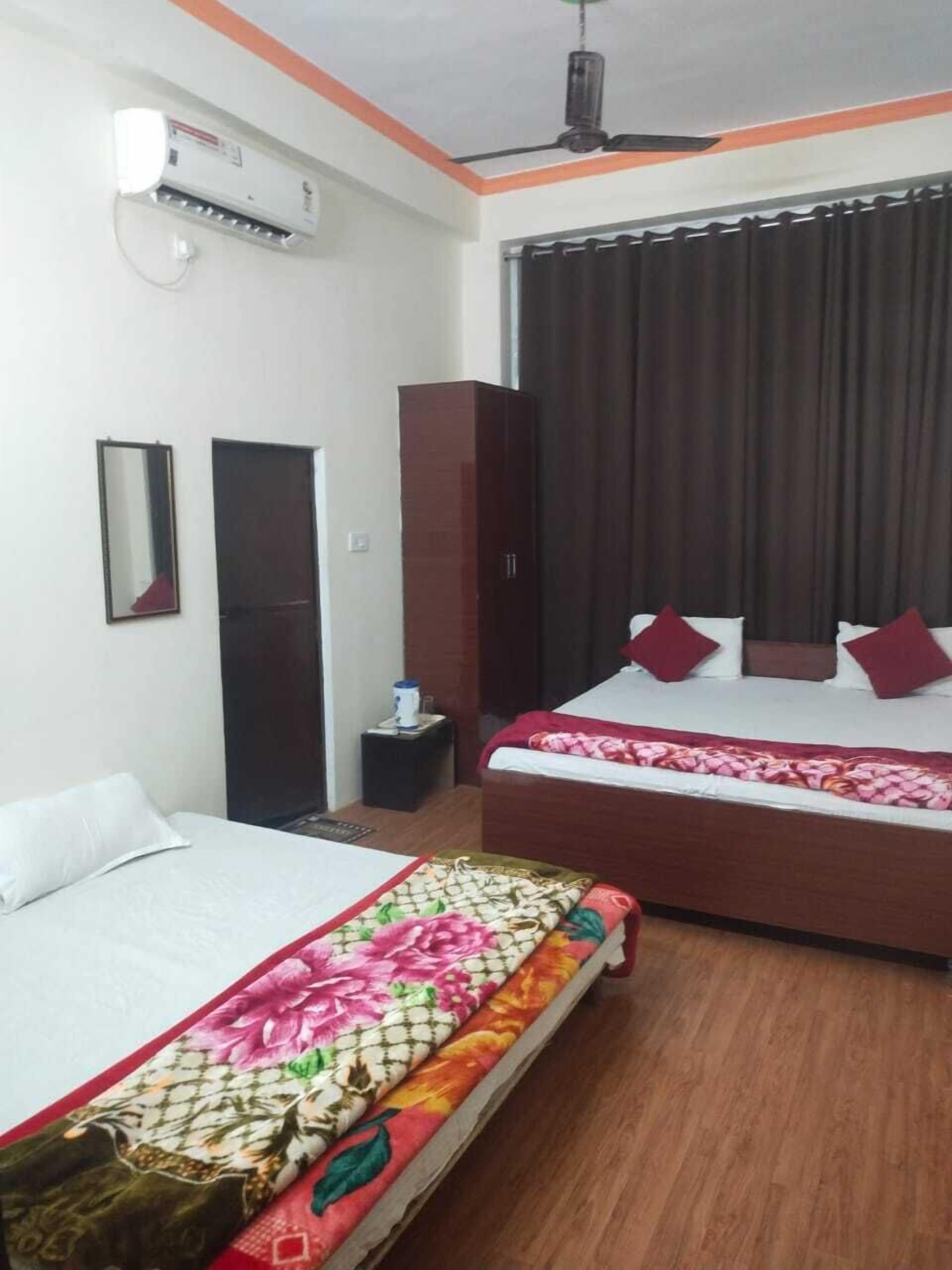 A hotel room with two beds, a ceiling fan, an air conditioning unit, a small table, and a dark-colored wardrobe.