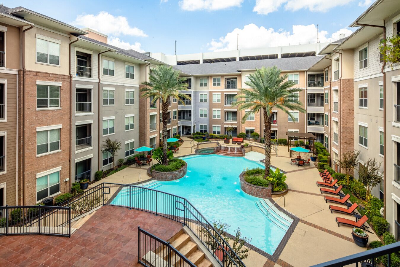 A multi-story hotel with a central swimming pool surrounded by palm trees and lounge chairs.