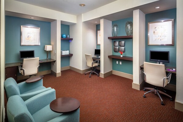 A hotel room with a seating area, two workstations, and artwork on the walls.