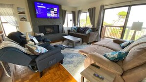 A living room with a flat-screen TV, a fireplace, a sofa, a coffee table, and a balcony with curtains.