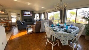 A spacious living area with a dining table set for four, a sofa, and a television mounted on the wall.