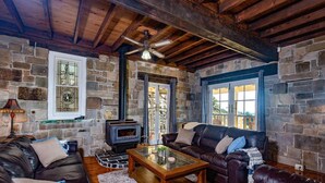 A cozy living room with stone walls, leather sofas, a wooden coffee table, and a fireplace. - Bimbadeen Mountain House - Valley views abound from this unique stone home (Mount View)
