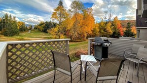 A deck with a grill, chairs, and a table overlooking a scenic view with autumn trees. - F39 Classy Bretton condo with AC, wifi, mountain views, updated bathrooms right on the golf course! (Bretton Woods)