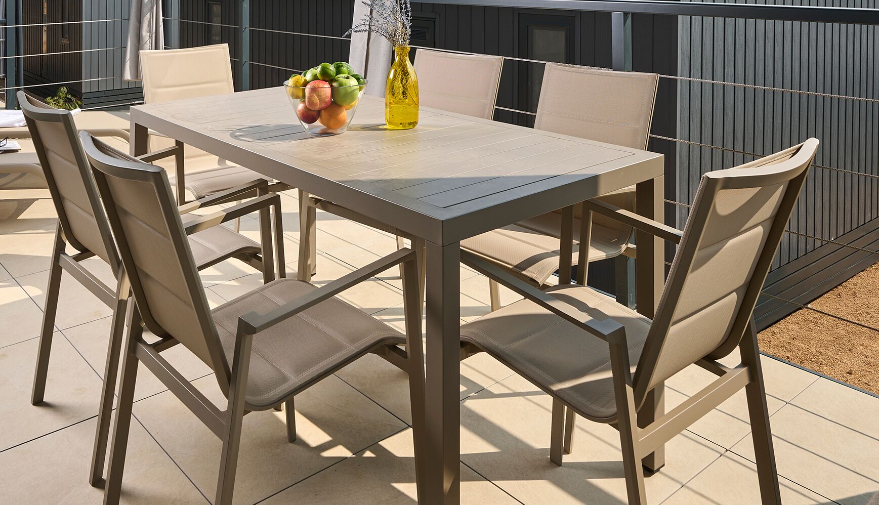 A patio table with chairs, a bowl of fruit, and a bottle of olive oil.