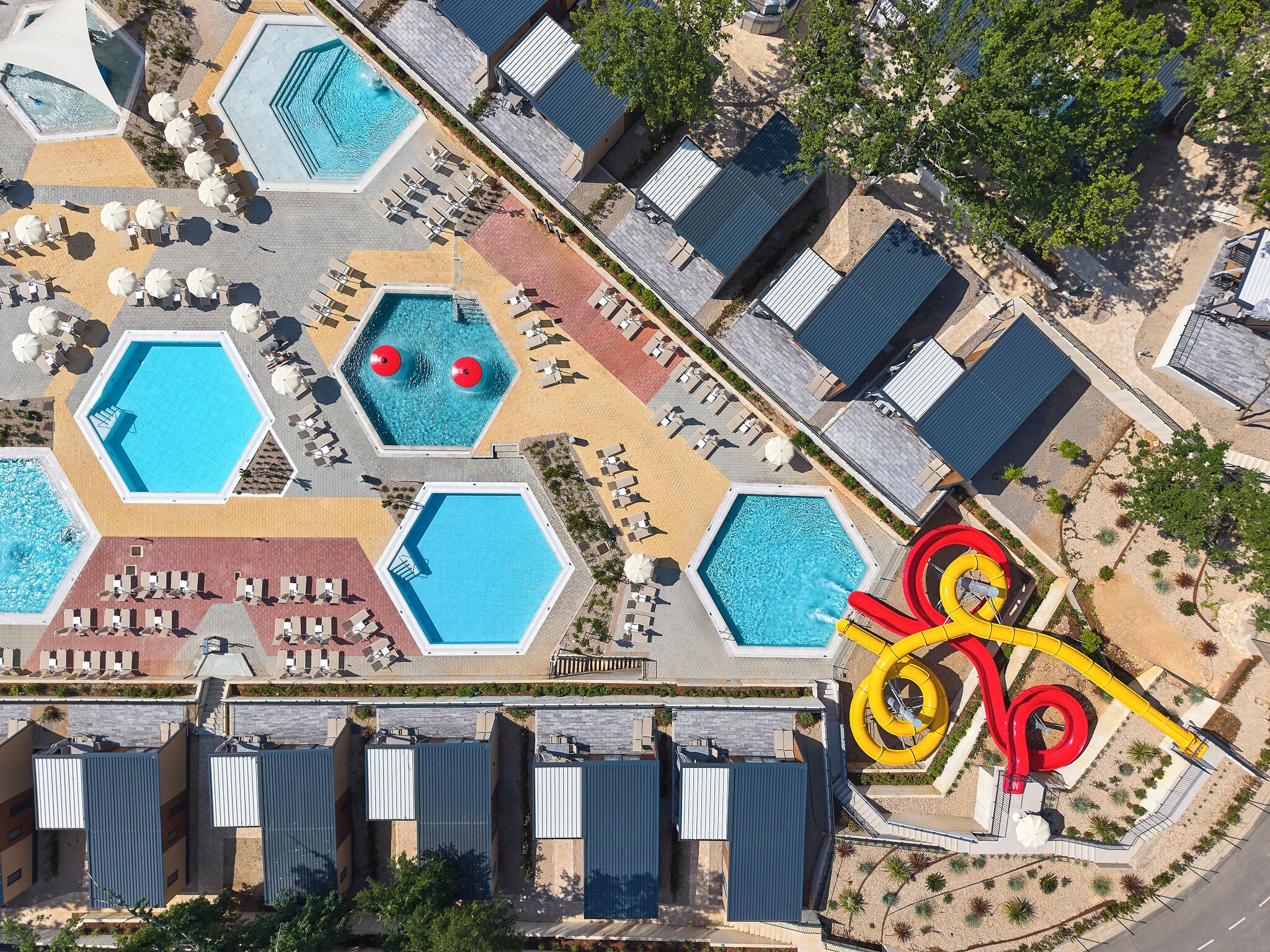 An aerial view of a resort with multiple swimming pools, sun loungers, and a water slide.