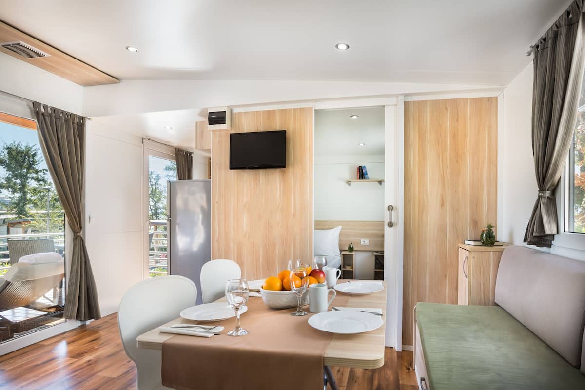 Un espace repas moderne avec une table dressée pour deux personnes, un réfrigérateur et un téléviseur fixé au mur.