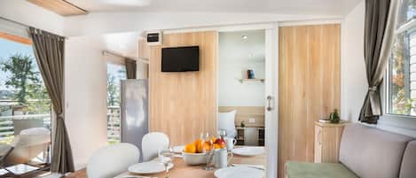 A modern dining area with a table set for two, a refrigerator, and a television mounted on the wall.