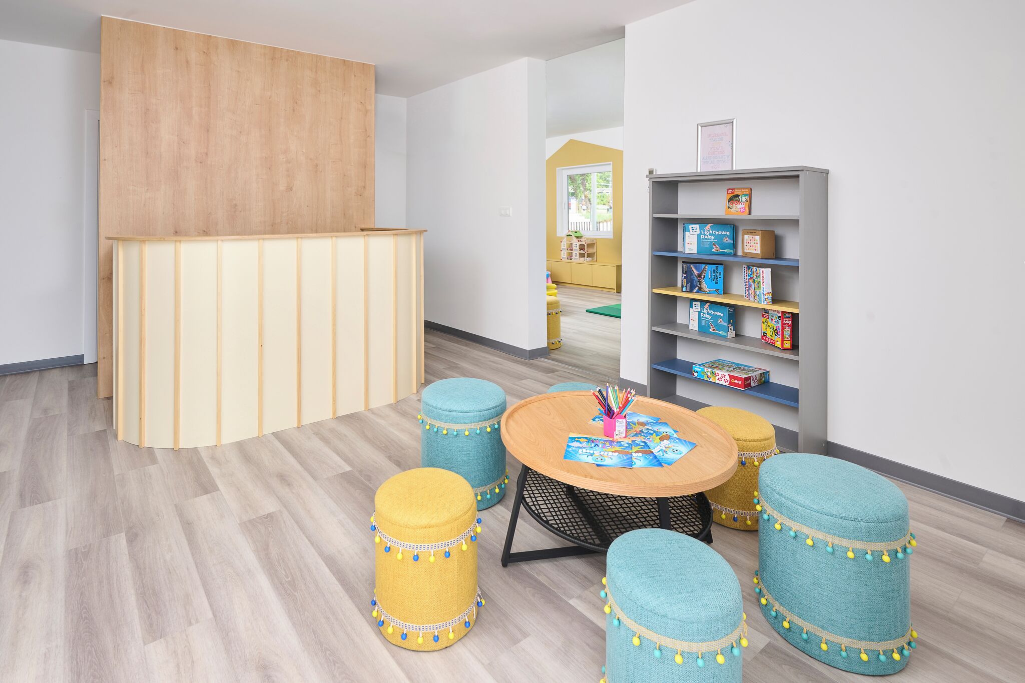 Een kinderspeelruimte met een ronde tafel, poefs, een boekenkast en een houten scheidingswand.