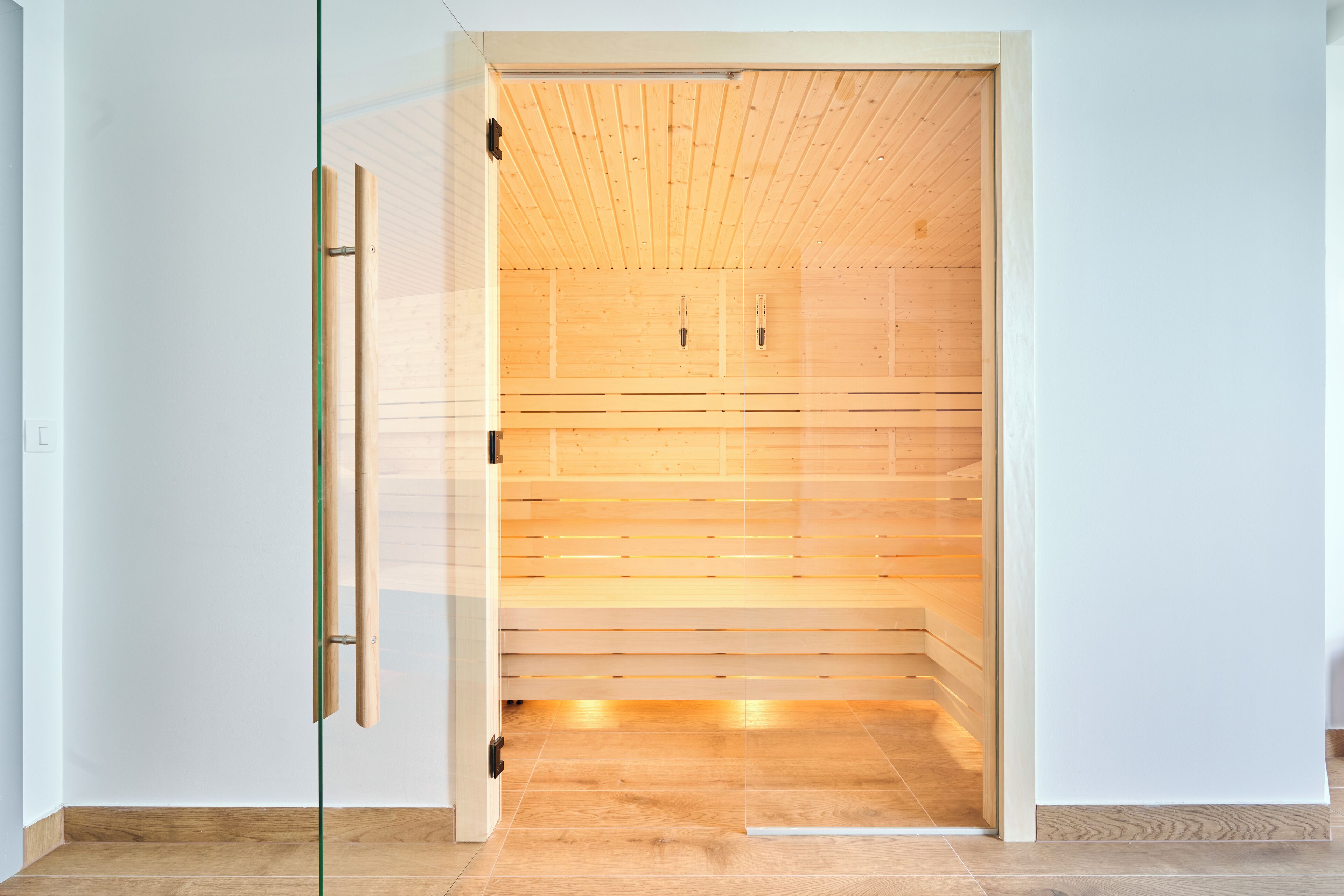 A wooden sauna with a glass door, wooden floor, and a simple, clean design.