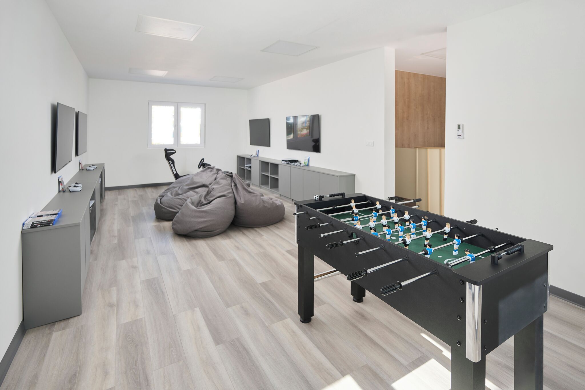 Una habitación moderna con mesa de fútbol de mesa, un sillón tipo orejero, un televisor y un escritorio con ordenador.