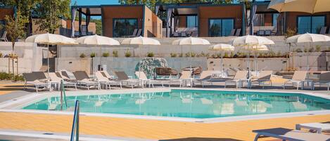 A swimming pool with lounge chairs and umbrellas, surrounded by modern buildings and trees.
