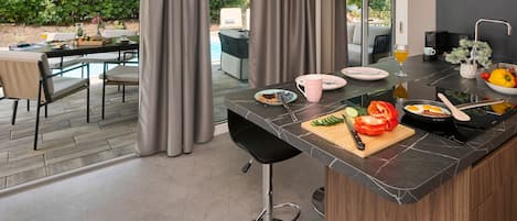 A modern kitchen with a marble countertop, a dining area with a glass table, and a view of the outdoors.