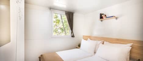 A neatly made bed with white linens, a wooden headboard, and a small bedside table with a book and a plant.