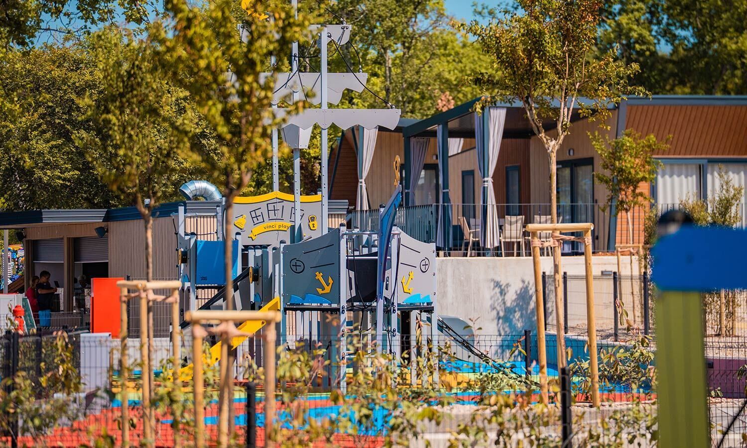 Un terrain de jeux doté de diverses installations, notamment un mur d’escalade et un toboggan, entouré de bâtiments et d’arbres.