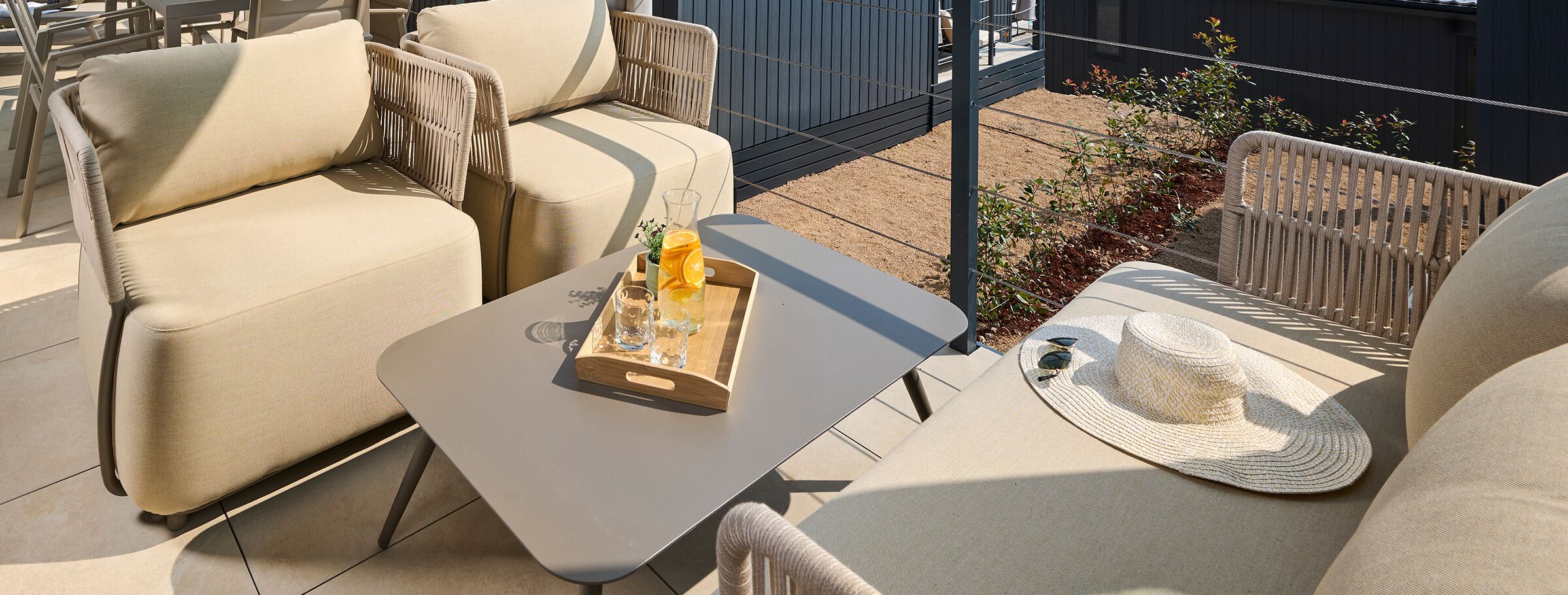 An outdoor seating area with cushioned chairs and a table, a woven basket, and a straw hat.