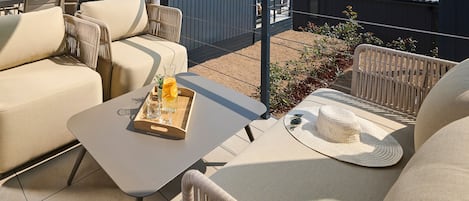 An outdoor seating area with cushioned chairs and a table, a woven basket, and a straw hat.