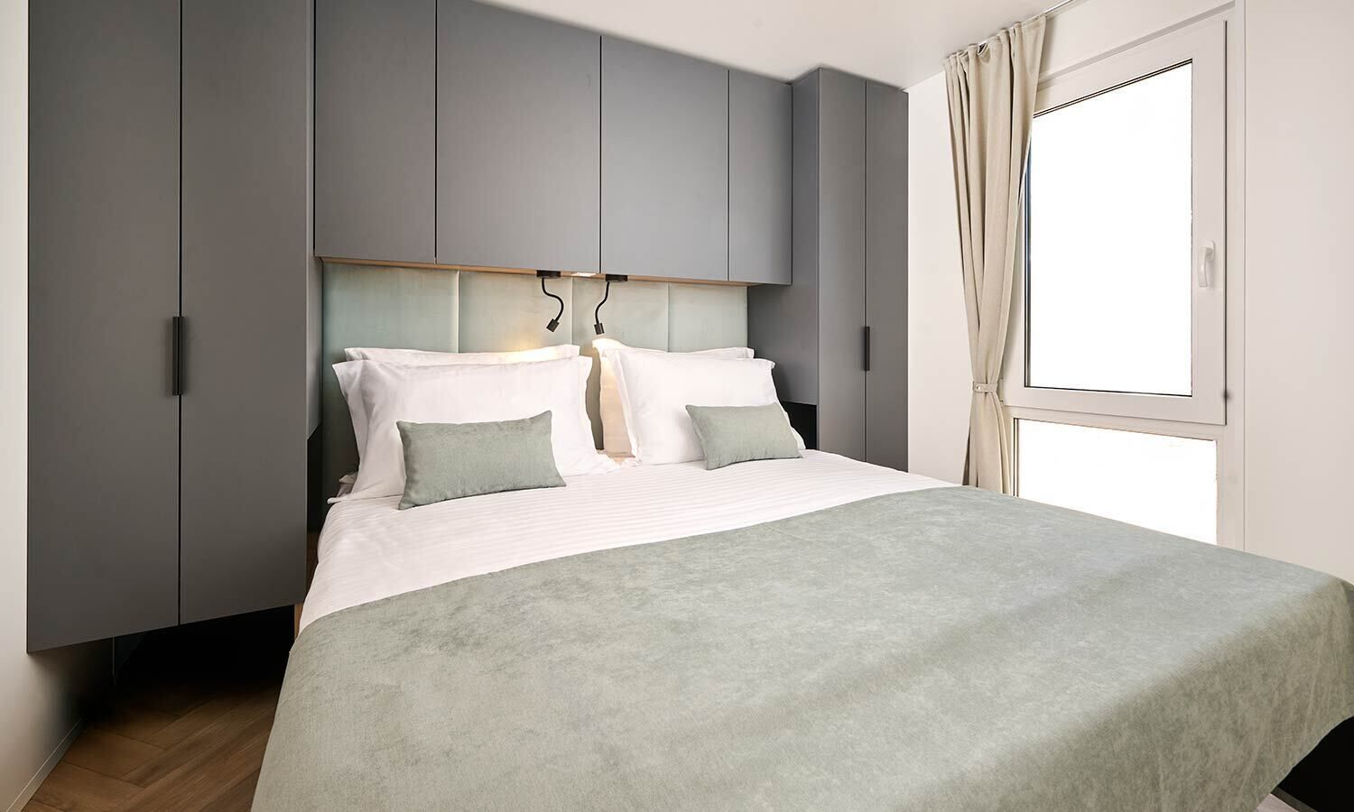 A modern bedroom with a bed, grey wardrobe, and a window with curtains.