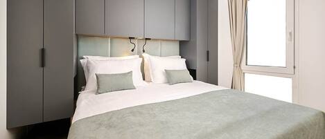 A modern bedroom with a bed, grey wardrobe, and a window with curtains.