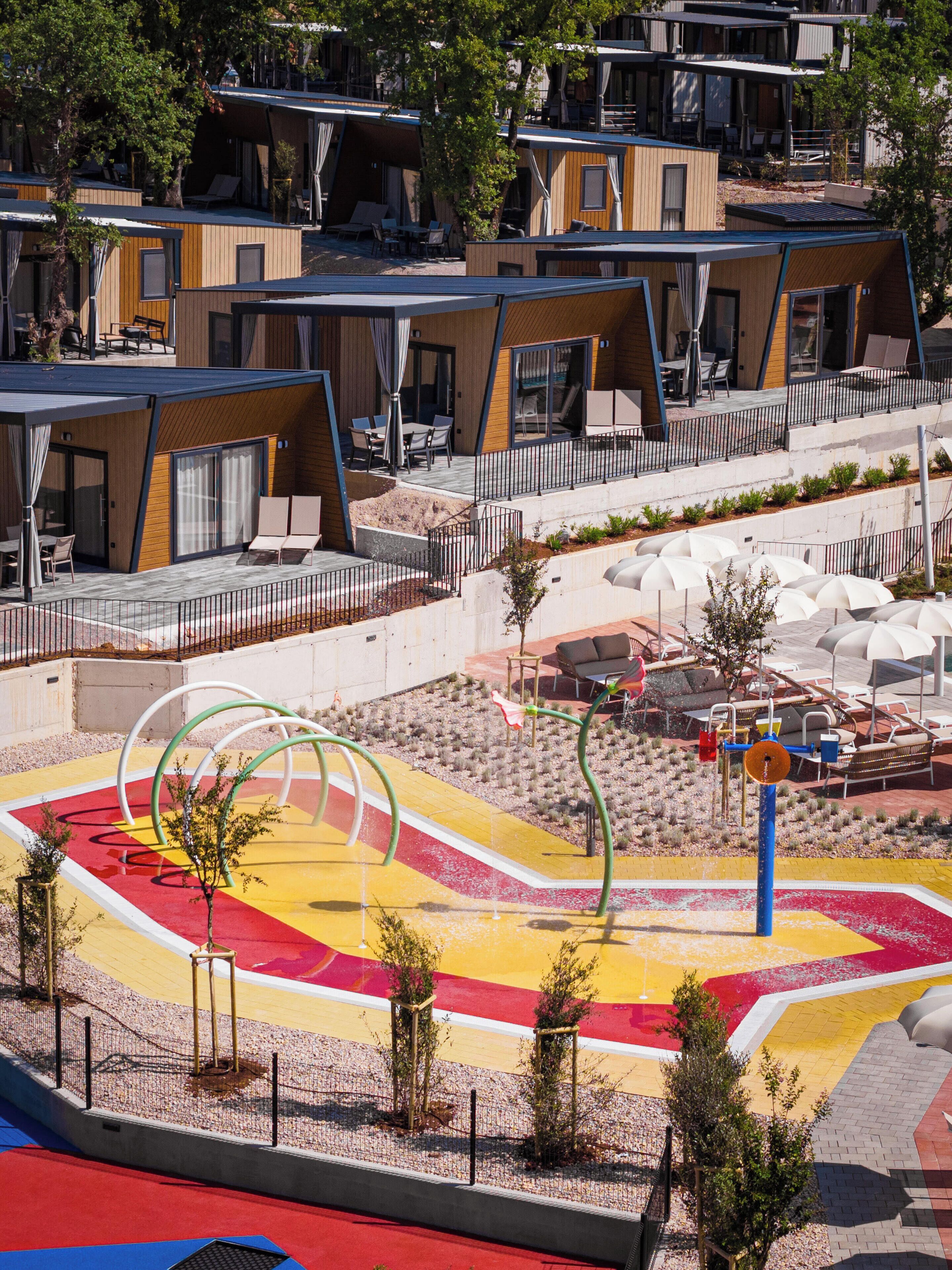 A modern outdoor area with a colorful play structure, seating areas, and a pool.