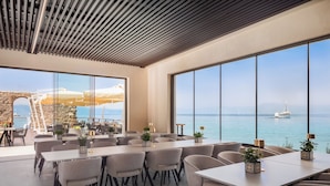 A modern dining area with large windows overlooking the sea, featuring a long table with chairs and potted plants. - Aminess Style Glamping Villas & Holiday Homes Atea (Omisalj)