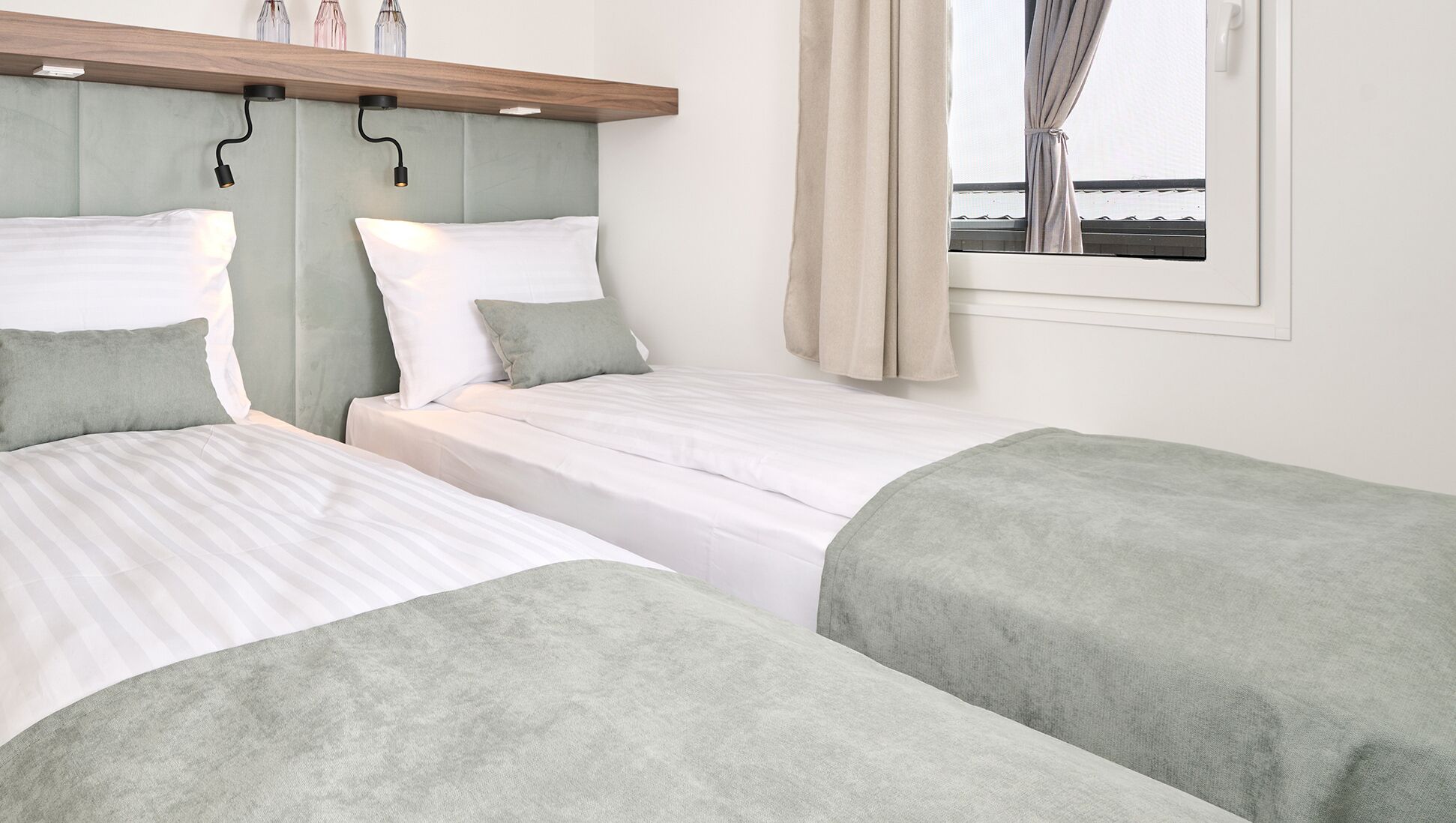 A hotel room with two beds, a headboard, a window with curtains, and a view of the sea.