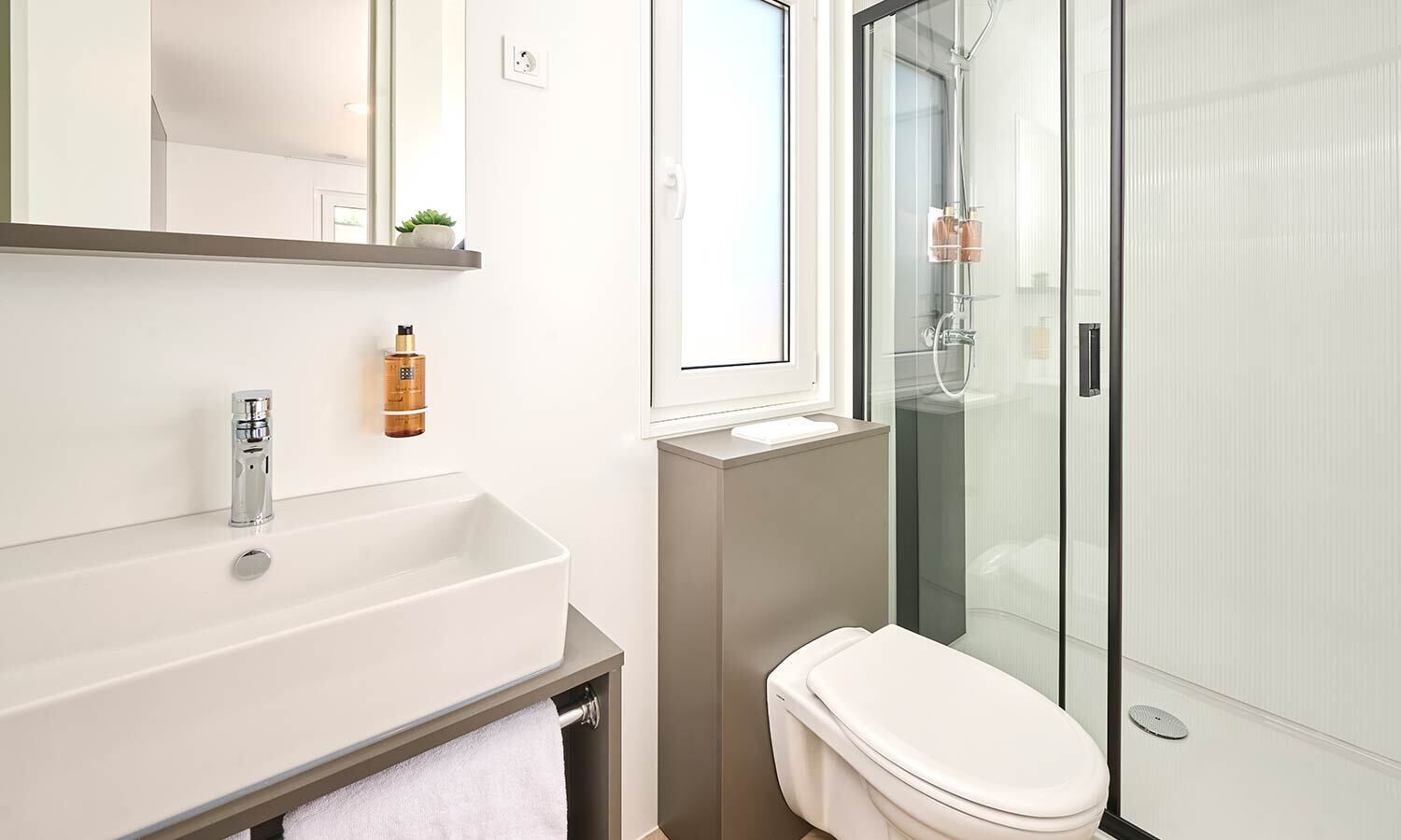 A modern bathroom with a white sink, a toilet, and a glass shower enclosure.