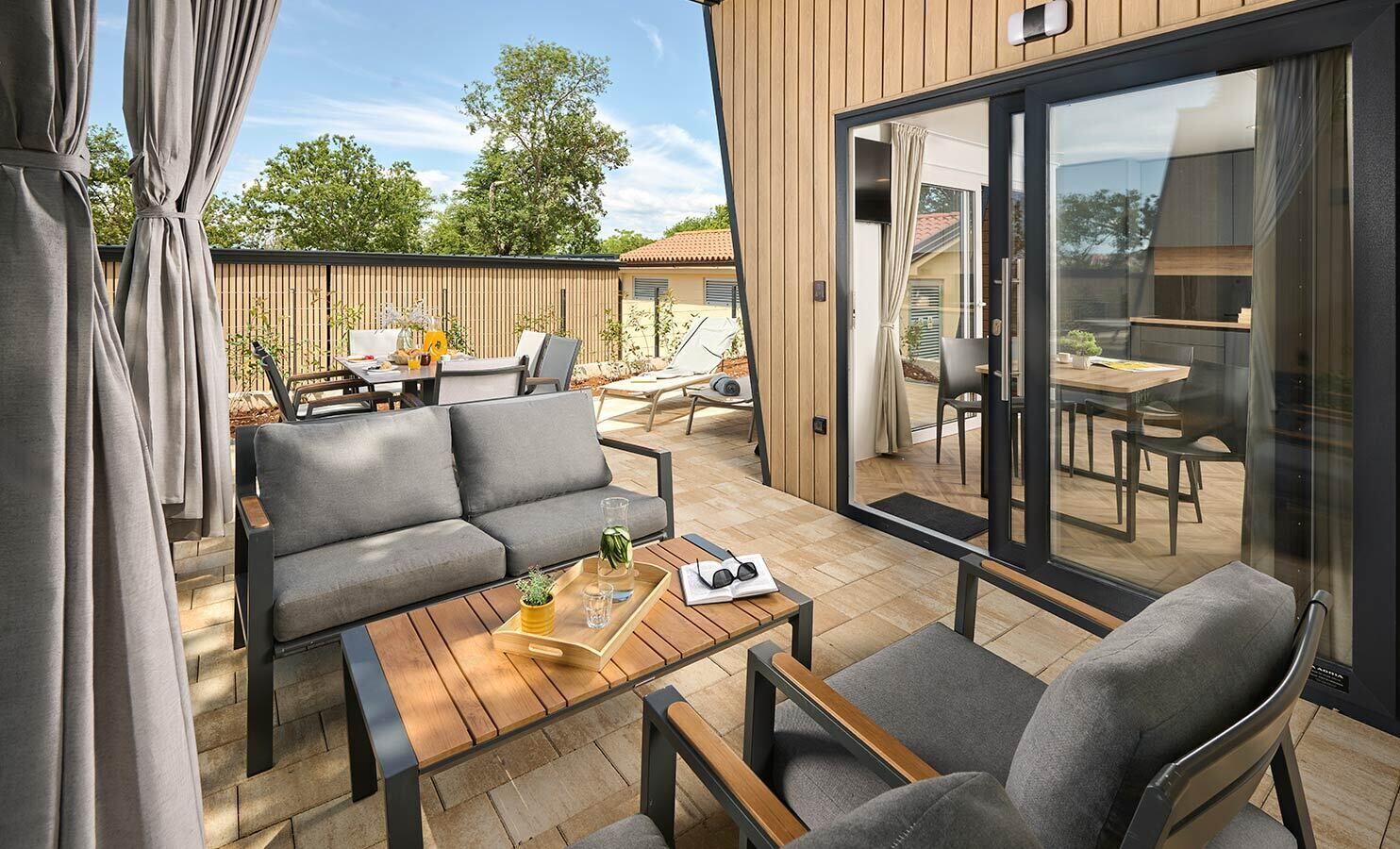 Een modern terras buiten, met een bank, stoelen en een houten tafel.