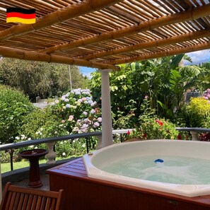 A hot tub on a balcony with a bamboo pergola overhead, surrounded by lush greenery and flowers.