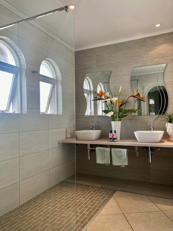A modern bathroom with two sinks, a large mirror, and a shower area.