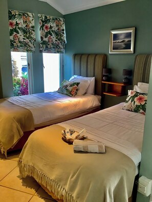 Une chambre d’hôtel avec deux lits, une fenêtre avec des rideaux, un tableau encadré au mur et une petite étagère avec quelques objets.