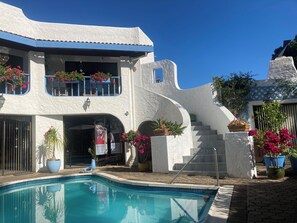 A white building with a pool, a balcony with flowers, and a staircase.