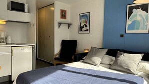 A hotel room with a bed, a desk with a microwave, a chair, and artwork on the walls.