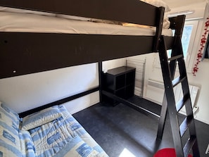 Uma cama box com escada, uma prateleira pequena e uma janela com vista.
