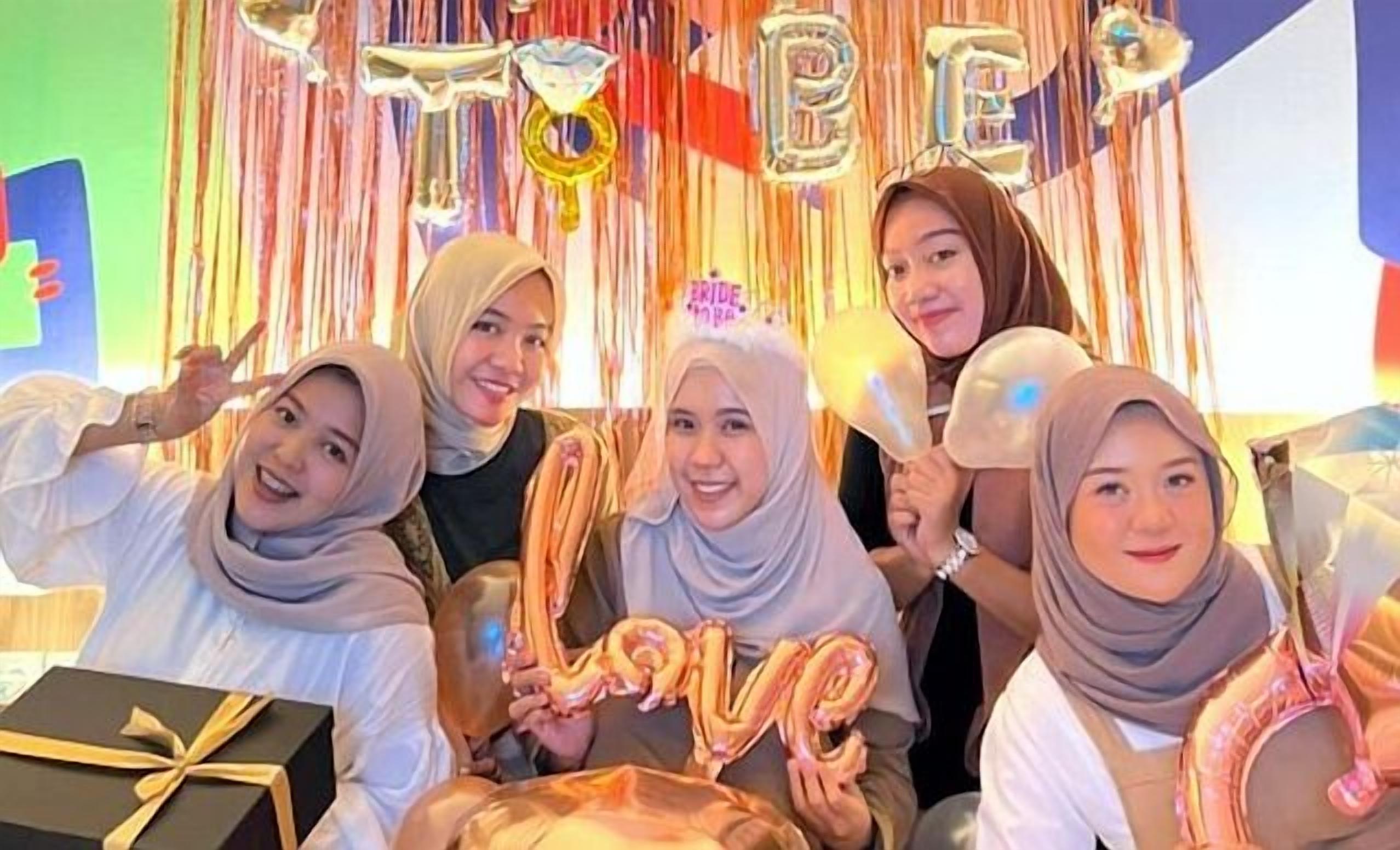 A group of people at a celebration with a backdrop that includes the words "LOVE" and "BRIDE."