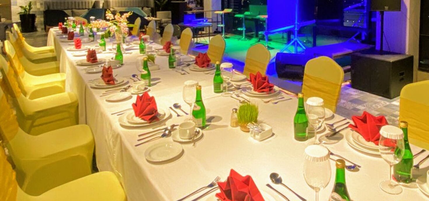 Een feestzaal met lange tafels gedekt voor een formeel evenement, met keurig opgemaakte zitplaatsen en stoelen.