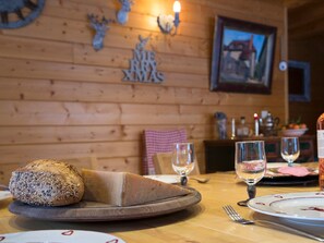 Ein rustikales Interieur mit einem Holztisch, Brot, Weingläsern und einer Weihnachtsdekoration an der Wand.