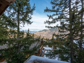 A mountainous landscape with snow-covered trees and a wooden cabin with a wooden deck.