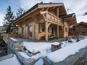 Eine Holzhütte mit Steinuntergrund, einem Balkon und einer Steinsäule, die das Anwesen umgibt.