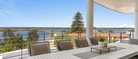 A balcony with a view of the sea, a table with chairs, and a potted plant.