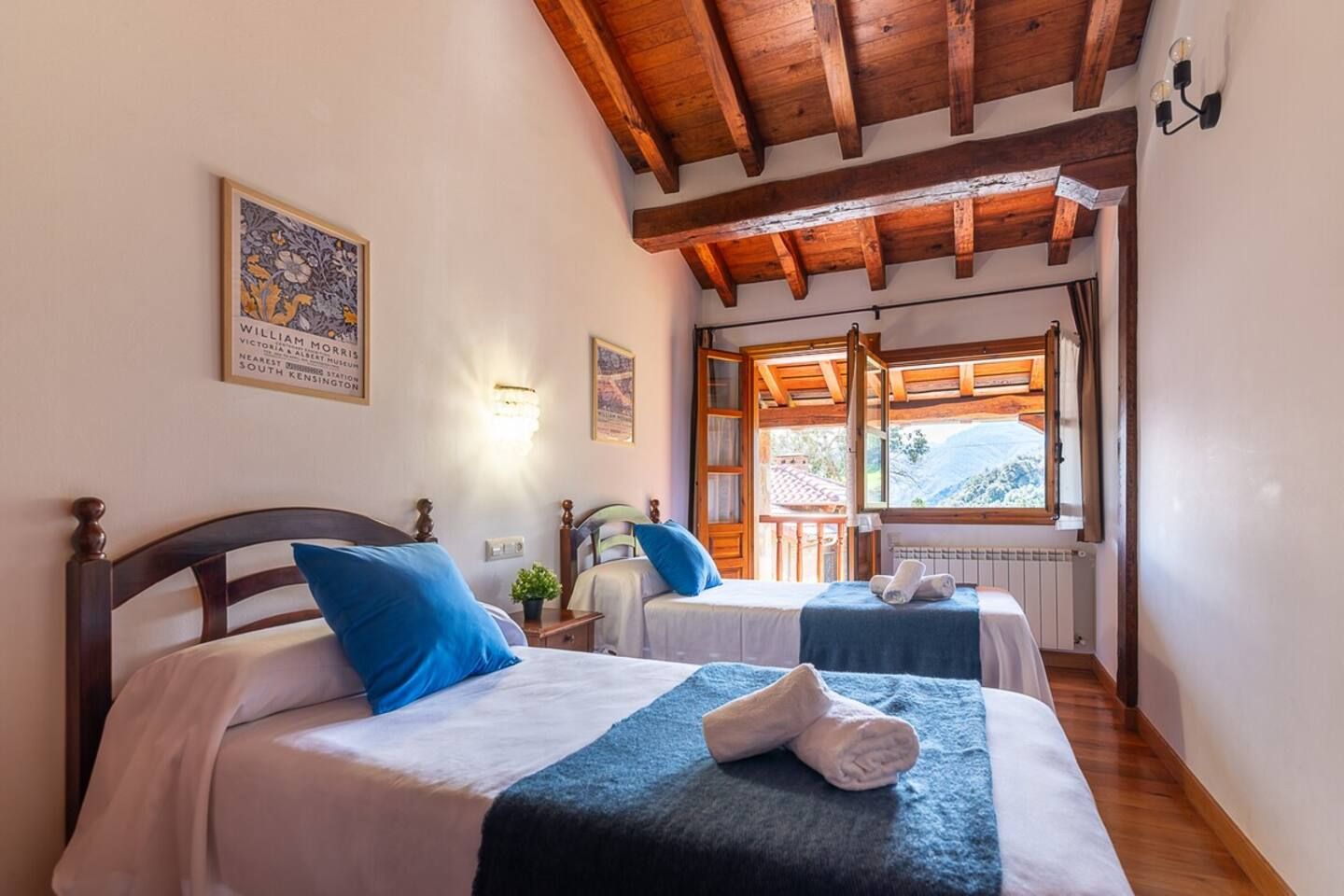 Une chambre avec deux lits, des poutres en bois au plafond, une fenêtre avec vue et un luminaire fixé au mur.