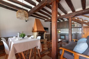 Een eetruimte met een tafel gedekt voor twee personen, een hanglamp en een stenen open haard.