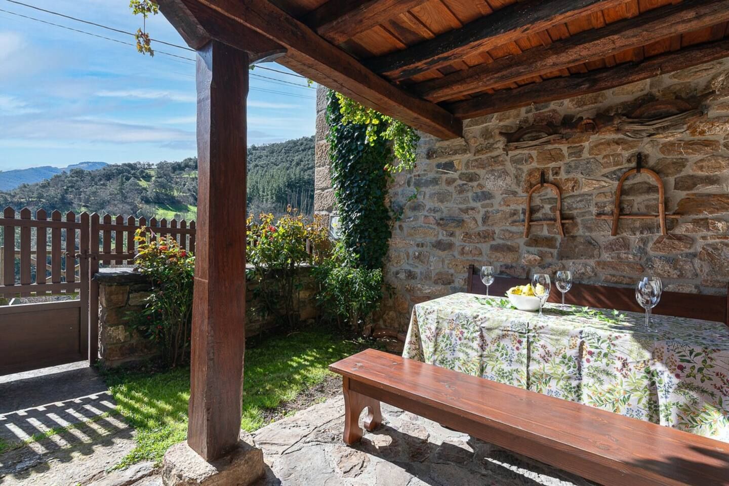 Un mur de pierre avec un banc en bois et une table dressée pour le repas, le tout surplombant un paysage montagneux.