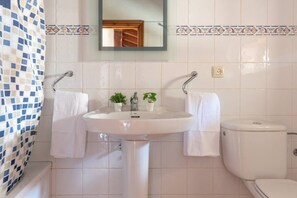 Een badkamer met een witte wasbak, twee planten in potten, een spiegel en een toilet.