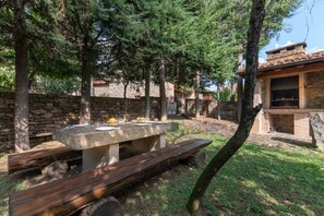 An outdoor dining area with a stone table and benches, surrounded by trees and a stone wall. - Fidalsa House of Views (Cabezón de Liébana)