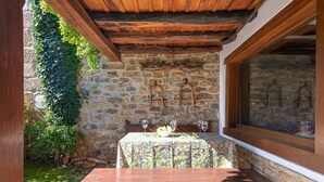 Un muro de piedra con un banco y una mesa de madera, una ventana con botellas, y un arco de piedra.