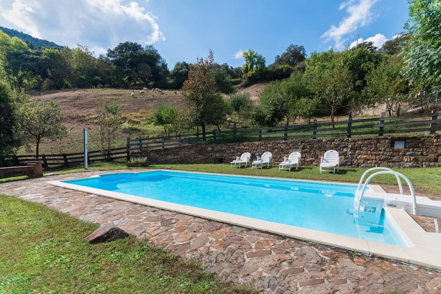 Une piscine dotée d’une plage en pierre, entourée d’un mur de pierre et d’une clôture en bois.